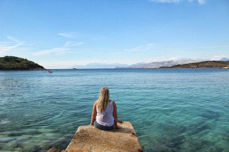what it's like living in Albania, person sitting on stone pier looking out across blue sea with mountains in distance