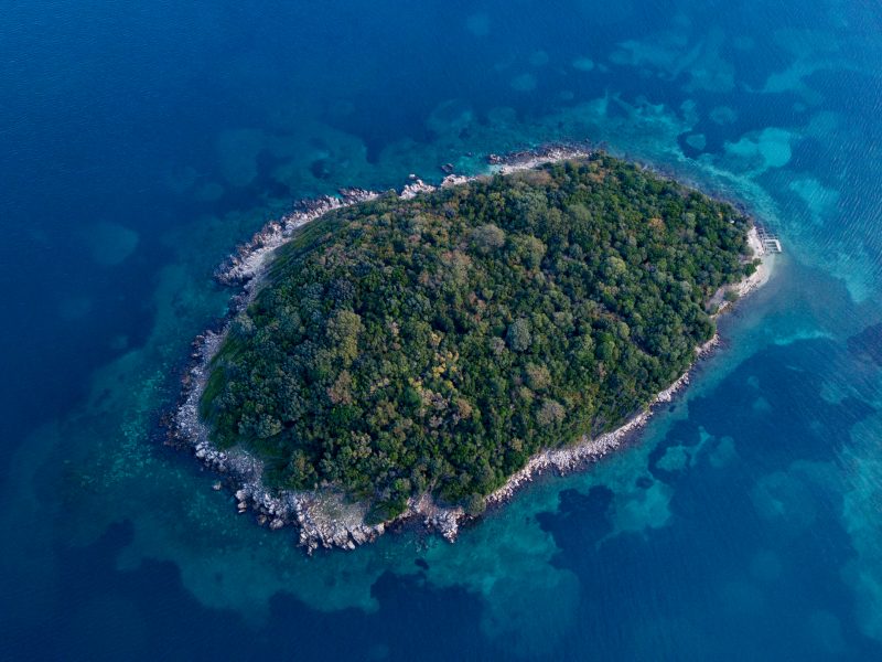 Your Local Guide to Ksamil, Albania, aerial shot of island covered in green foliage surrounded by clear blue water